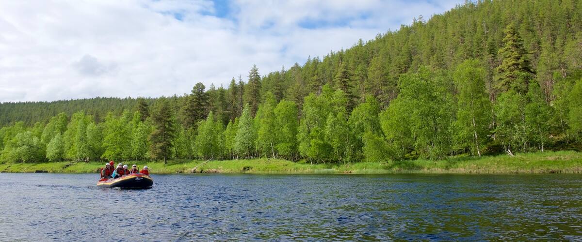 A group of people on a raft on a calm river, surrounded by dense green forest and a clear blue sky.