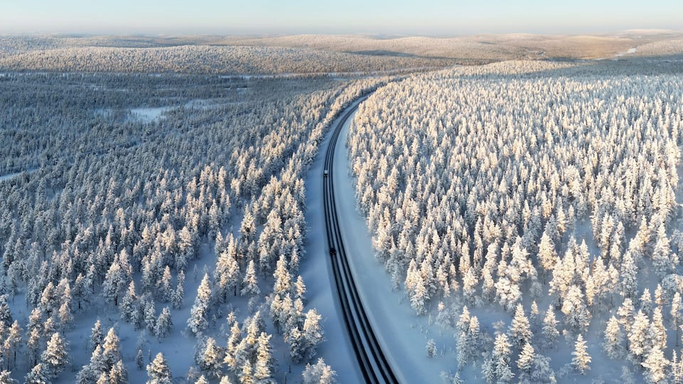 An aerial view of a snow-covered forest with a winding road.