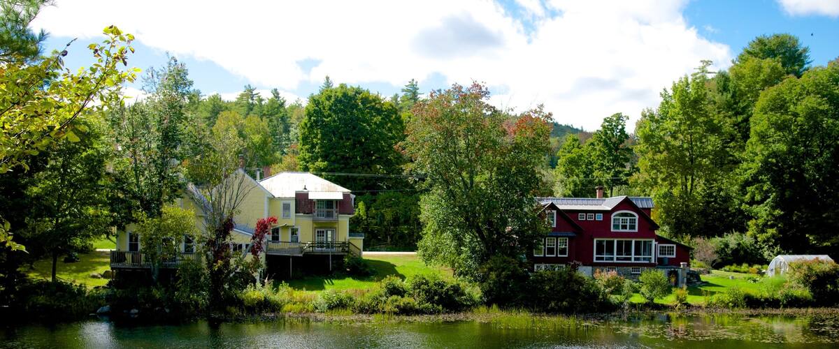 Two houses by a calm lake surrounded by lush greenery and trees.