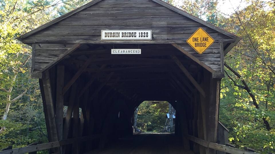 A wooden covered bridge with signs reading "Durgin Bridge 1828" and "Clearance 93".