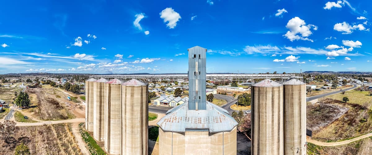 A grain silo complex with a central tower and four surrounding silos, set against a rural landscape with a clear sky.