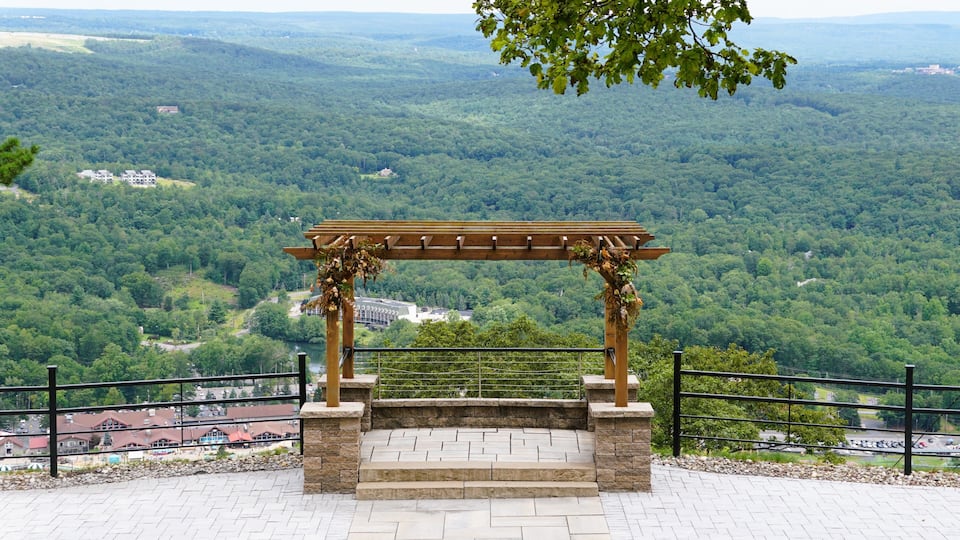 A wooden pergola with stone steps overlooking a forested valley.