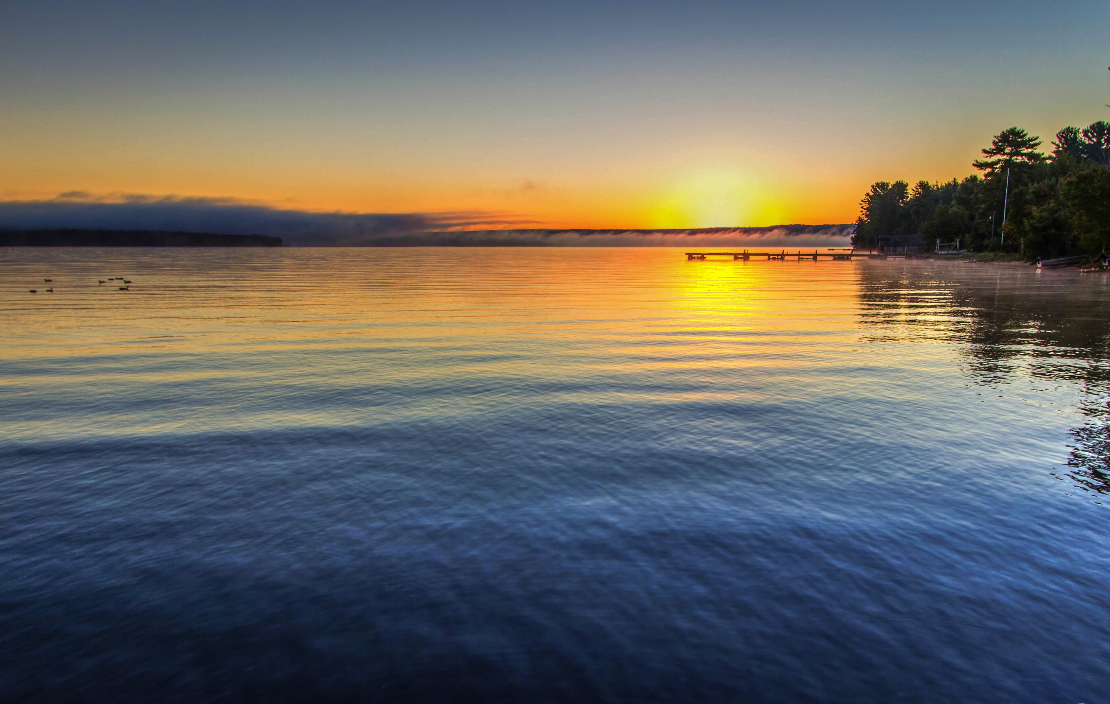 Foggy Summer Lake Sunrise Panorama. Sunrise over Lake Superior on a foggy summer morning with a small wooden dock at the horizon.