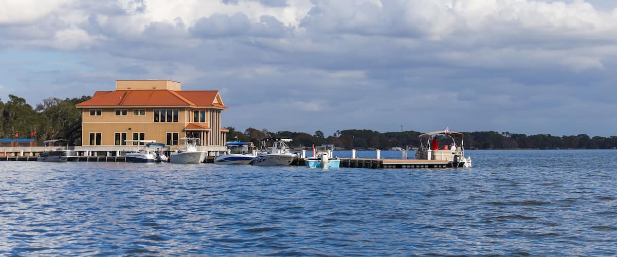 A waterfront with a large building, several boats docked, and a pier extending into the water.