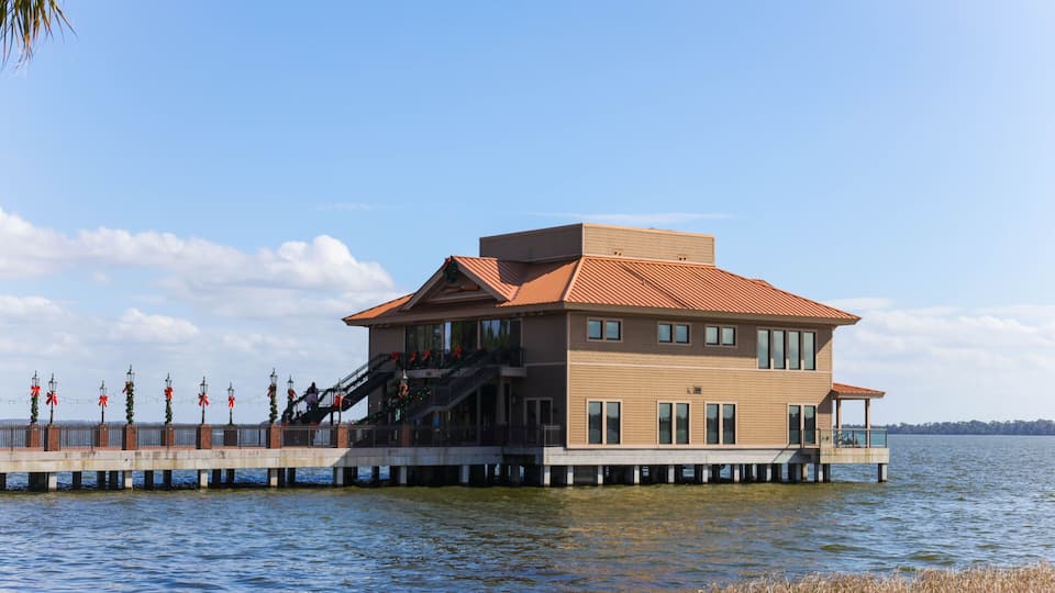 A waterfront house with a red roof, a dock, and a clear blue sky.