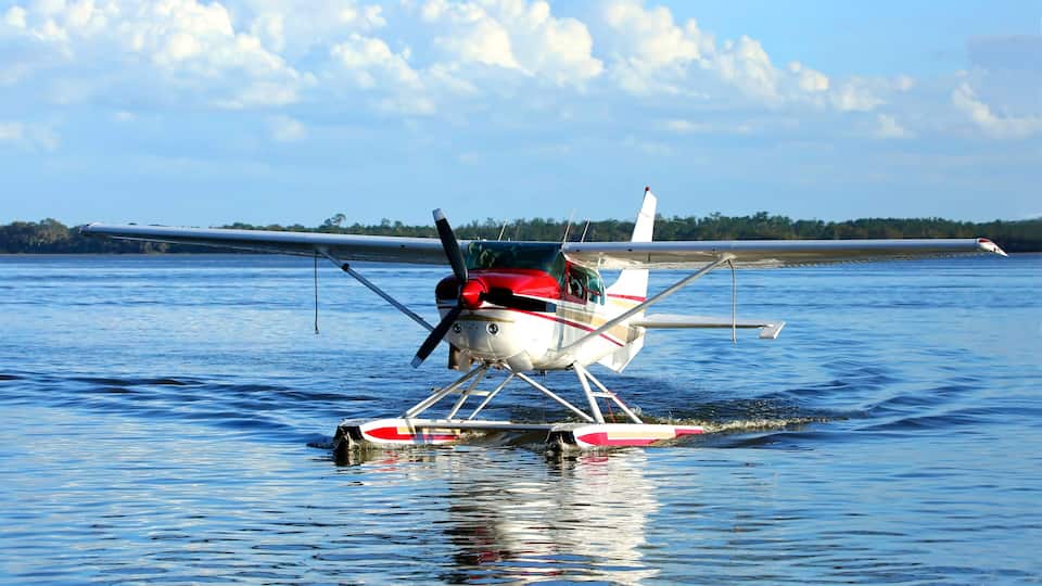 A seaplane on water with a clear sky and distant shoreline.