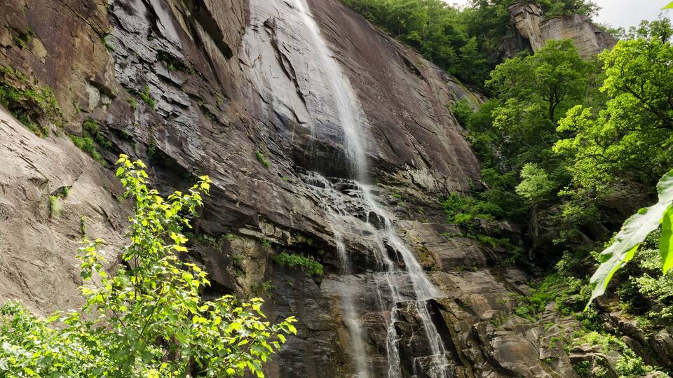 A waterfall cascading down a rocky cliff surrounded by lush greenery.