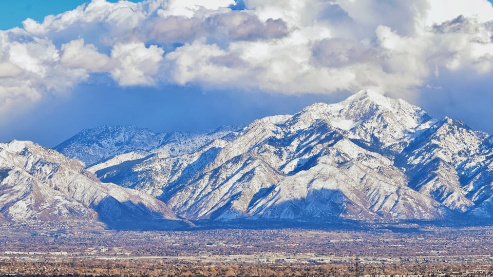 Snow-covered mountains, a cityscape, and a clear sky with clouds.