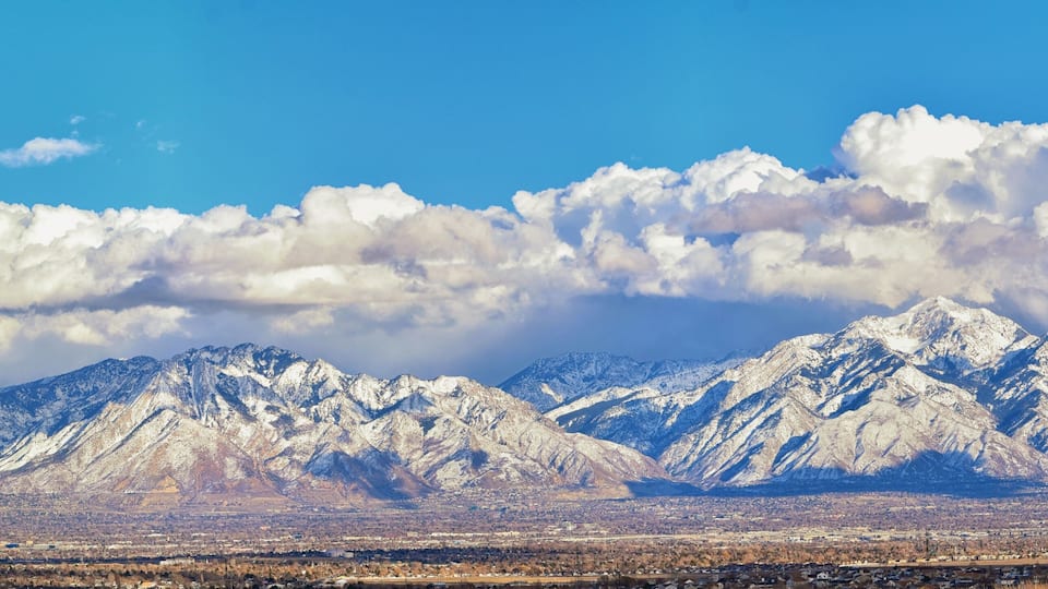 Snow-covered mountains, a clear blue sky, and a distant cityscape.