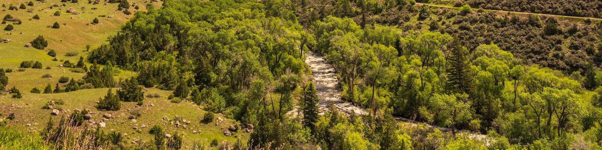 A mountainous landscape with a river flowing through a valley, surrounded by greenery and rocky cliffs.