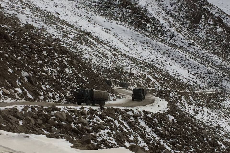 A snowy mountainous landscape with rocky terrain and two trucks on a dirt road.