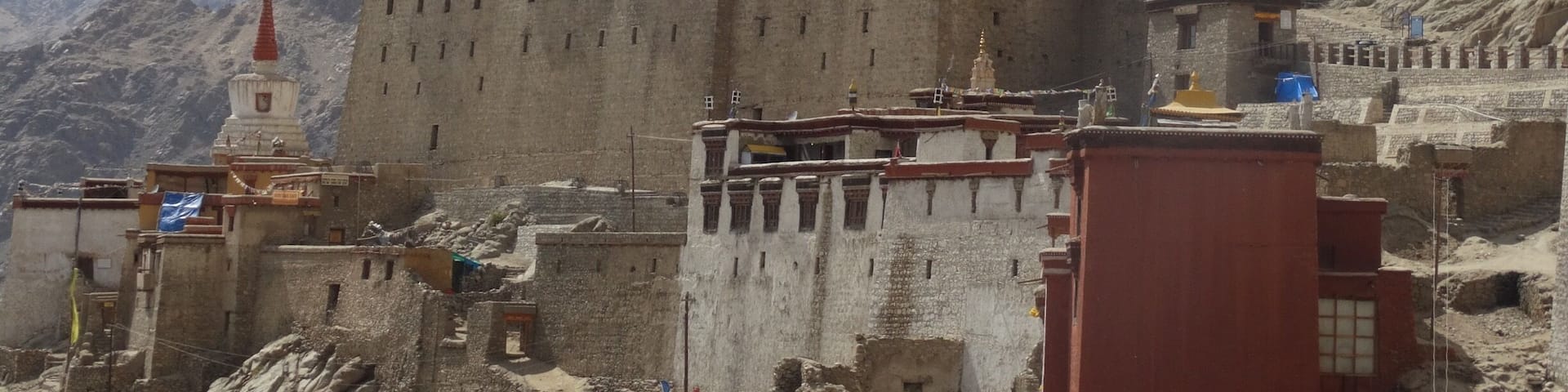 A large, multi-tiered monastery complex with traditional Tibetan architecture, set against a mountainous backdrop.