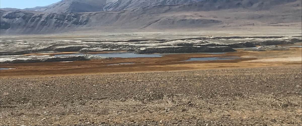 A barren landscape with a flat terrain in the foreground and a range of mountains in the background.