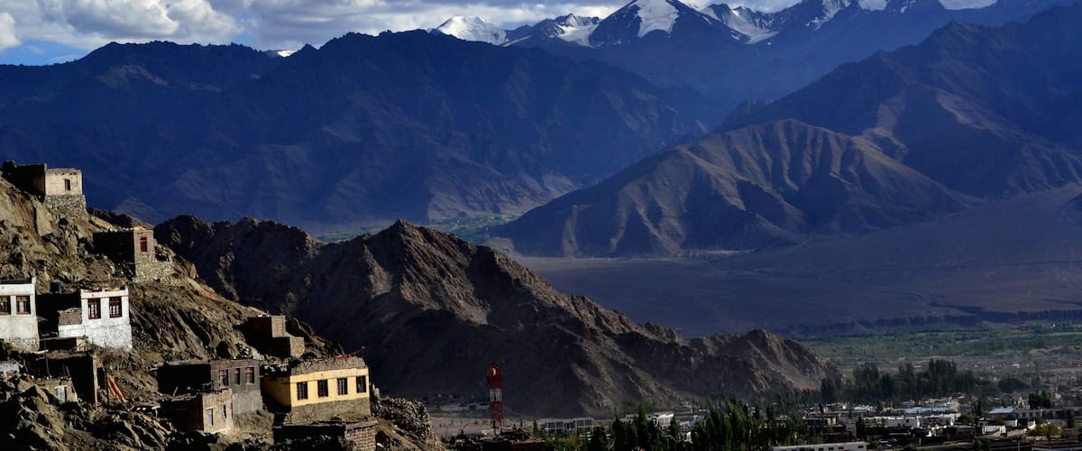 A mountainous landscape with snow-capped peaks, a village with traditional buildings, and a clear sky with clouds.