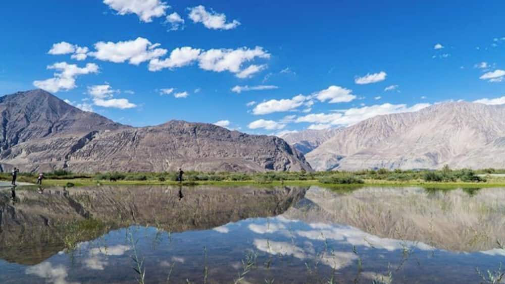A mountain range, a clear blue sky, and a calm lake with reflections.