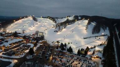 Aerial view of the illuminated ski slopes and base area of Crystal Mountain at night, featuring snow-covered terrain, chairlifts, and a busy parking lot in Thompsonville, Michigan, United States.