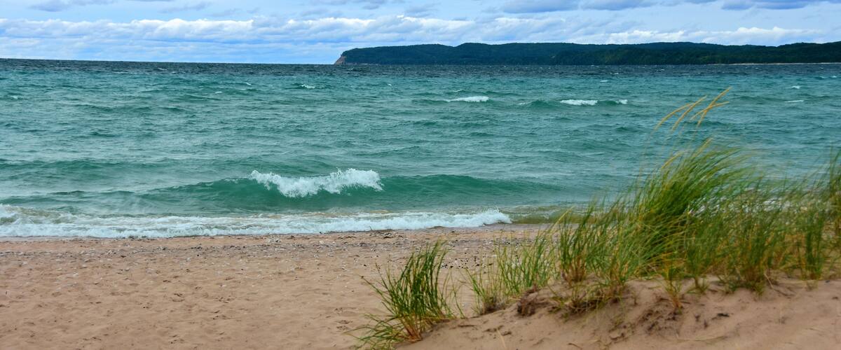 A beach with waves, sand, and grass.