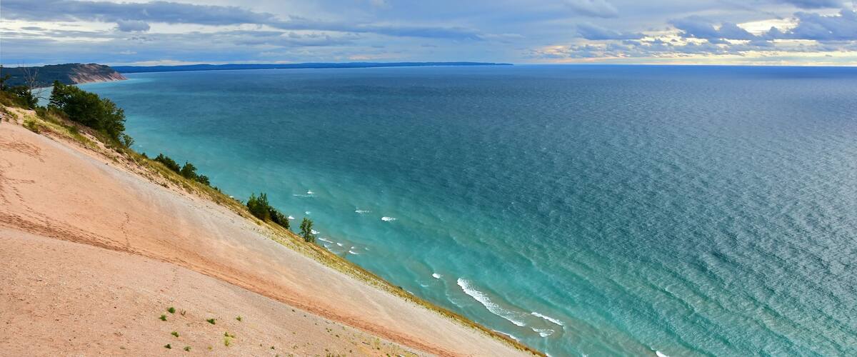 a stunning view across the turquoise-colored water of lake michigan and sand dunes from the lake michigan overlook in sleeping bear dunes national lakeshore in the lower peninsula of michigan
