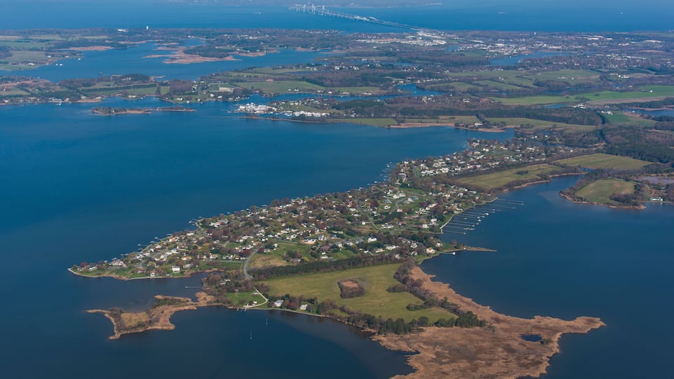 An aerial view of a coastal town with a long peninsula extending into the sea, surrounded by water and greenery.