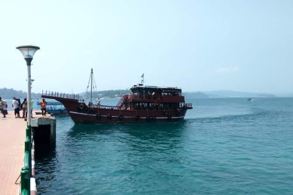 A large red boat docked at a pier with people walking along the pier.