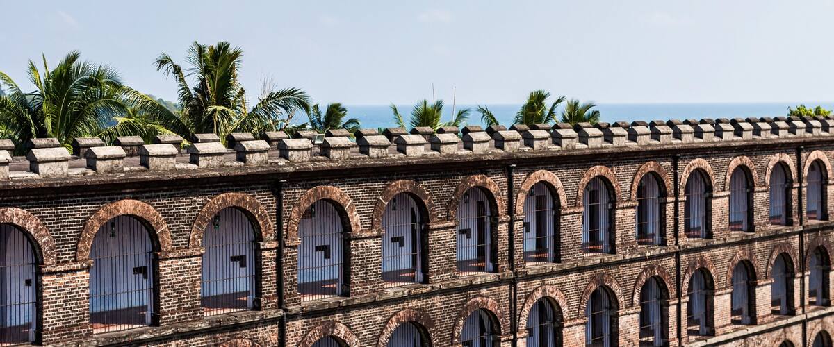 A brick building with arched windows and a tiled roof, surrounded by palm trees.
