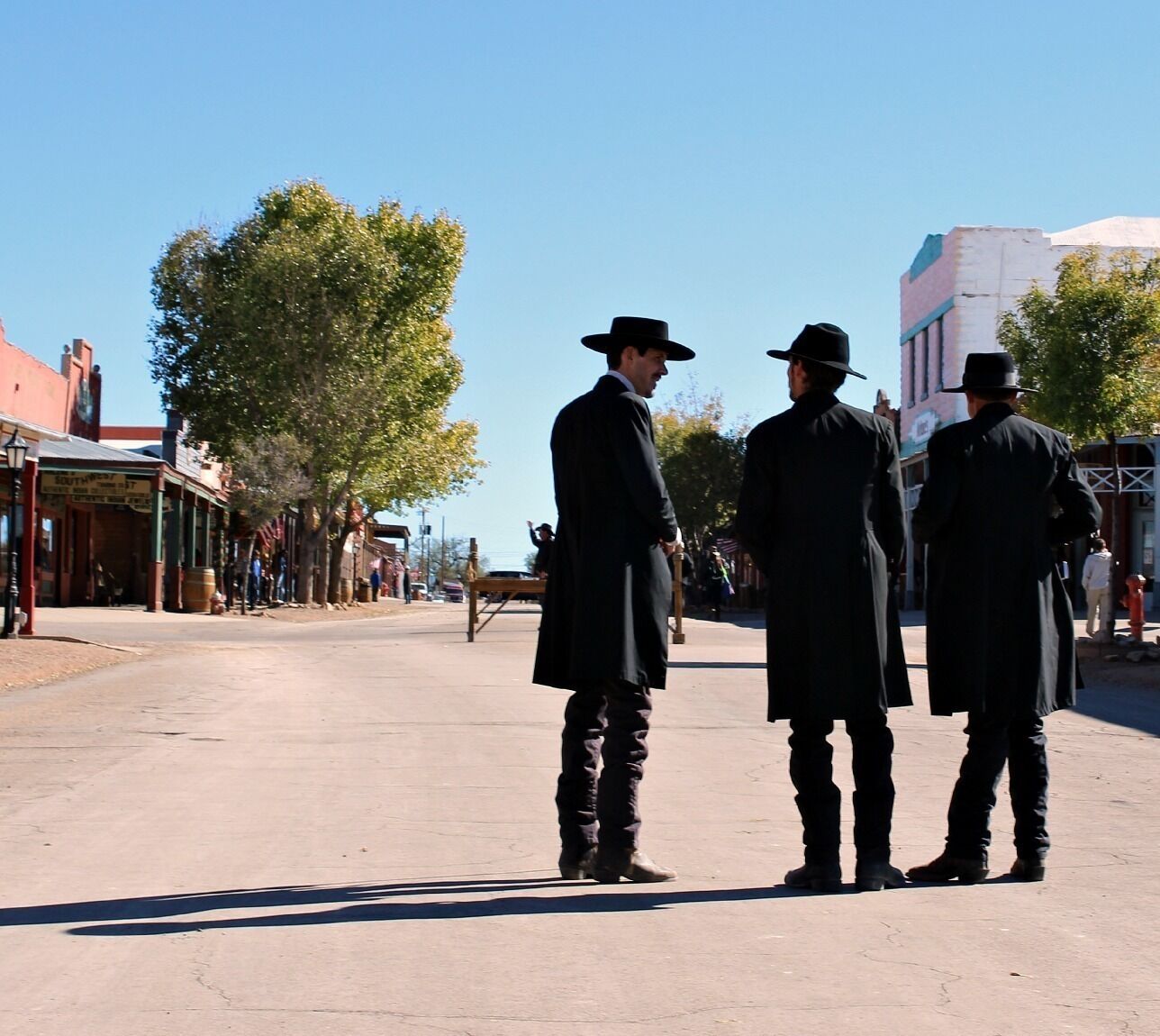 A street scene with three men in long coats and hats.