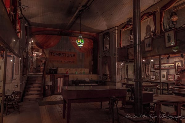 The Birdcage Theater is one of Tombstone's most authentic attractions and one of the West's most famous landmarks. Legend has it 26 people were killed in the Bird Cage during it reputed 8 years as one of the wildest and meanest places in Tombstone. Over 120 bullet holes remain in the building. The ladies of the night, plied their trade in cribs suspended from the ceiling in the building. 14 cribs lined the sides of the gambling hall, 7 on each side of the room. The ladies would pull the drapes to entertain their clients.
Within these walls once drank and played the likes of Wyatt Earp, Bat Masterson, and members of the Cowboy faction, and Doc Holliday, who dealt faro in the gambling parlor. On one occasion, while Doc was dealing, one of his hated rivals, Johnny Ringo, passed by the table. Doc then murmured, "Care to buck the tiger, Johnny? It's the gustiest game in town."
Upon hearing this, a drunken Ringo wheeled around, removed his bandana and said to Holliday,
"Care to grab to the other end of this bandanna? This is the deadliest game in town."
In those days when two men grabbed the opposite ends of a bandanna, they would then fire at each other at point-blank range, generally with both men winding up dead.
Undaunted, Doc simply stood smiling, ready to accept the challenge, but ready to use knives, rather than guns.
Curly Bill Brocius then interceded, grabbing Ringo and yelling, "Hell, Doc, he’s drunk!”
Doc, who had also been drinking, like usual, answered, "Brocius, I drink more by 10:00 a.m. than he can all day." Doc then turned and walked away.
One of its most famous distinctions was one of the longest running games of poker ever played. Seating seven players plus a dealer, the minimum buy-in was $1,000.00 and was played around the clock for, 8 years 5 months and three days.