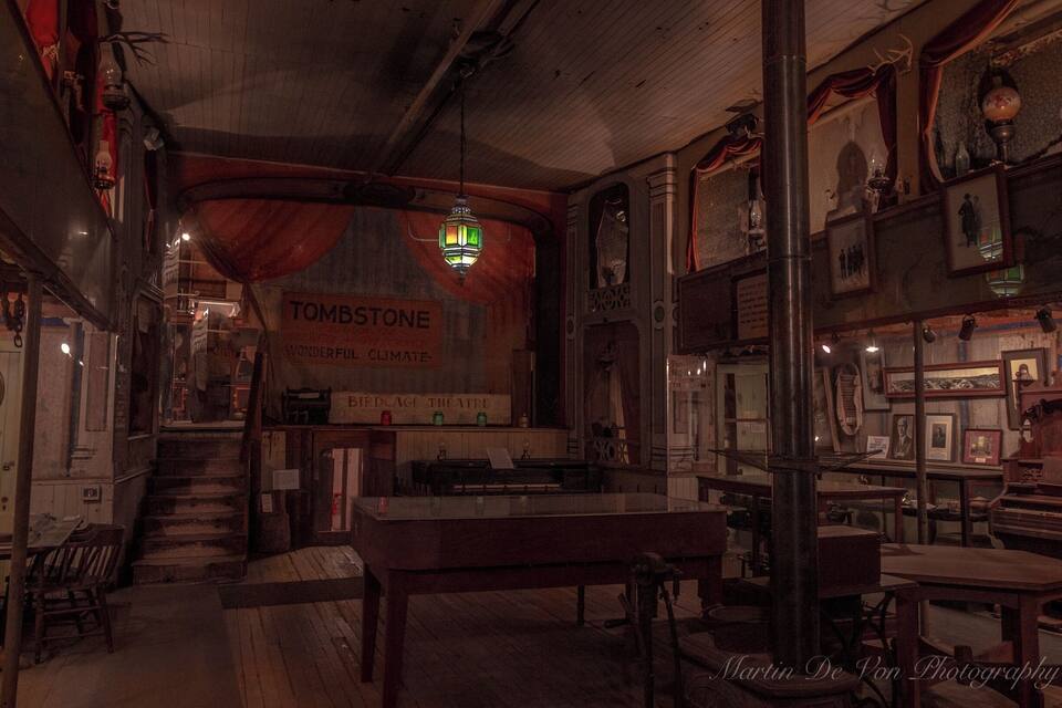 Un interior poc il·luminat amb mobles de fusta, una escala i un senyal que diu "TOMBSTONE".
