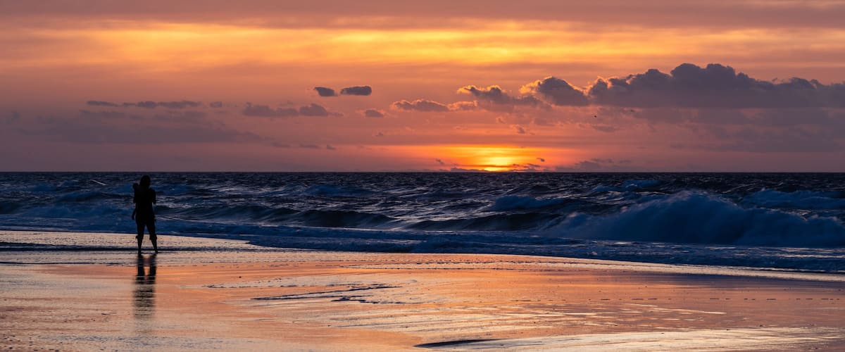 A sunset over the ocean with a person standing on the beach.