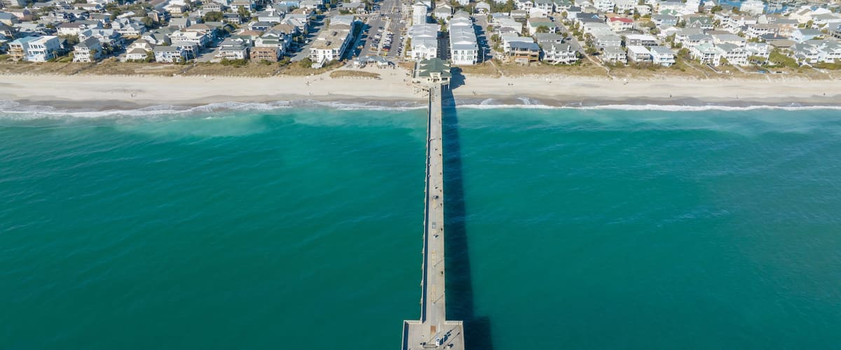 An aerial view of a coastal town with a long pier extending into the turquoise sea.