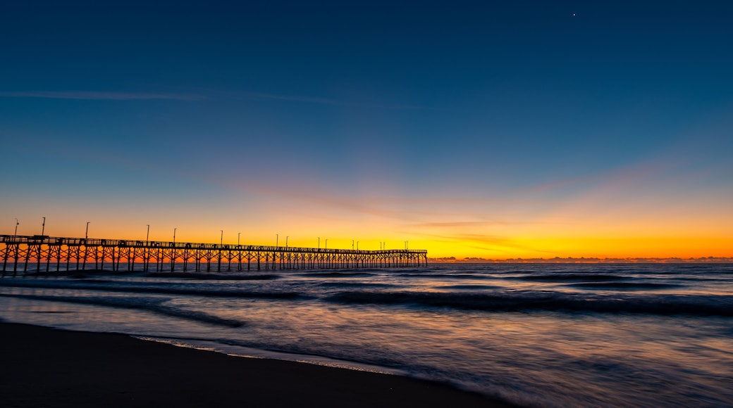 A pier extending into the ocean at sunset with waves gently lapping at the shore.