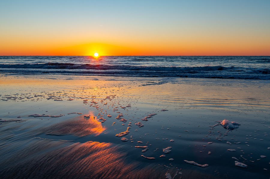 A sunset over a beach with waves and footprints in the sand.