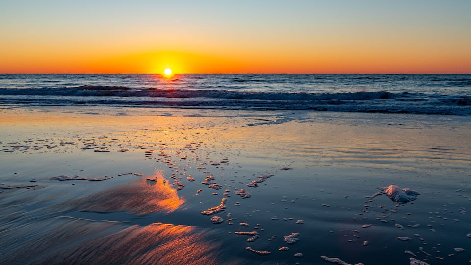 A sunset over a beach with waves and footprints in the sand.