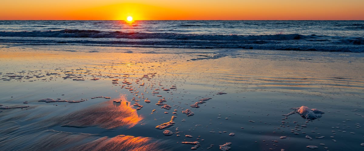 A sunset over a beach with waves and footprints in the sand.