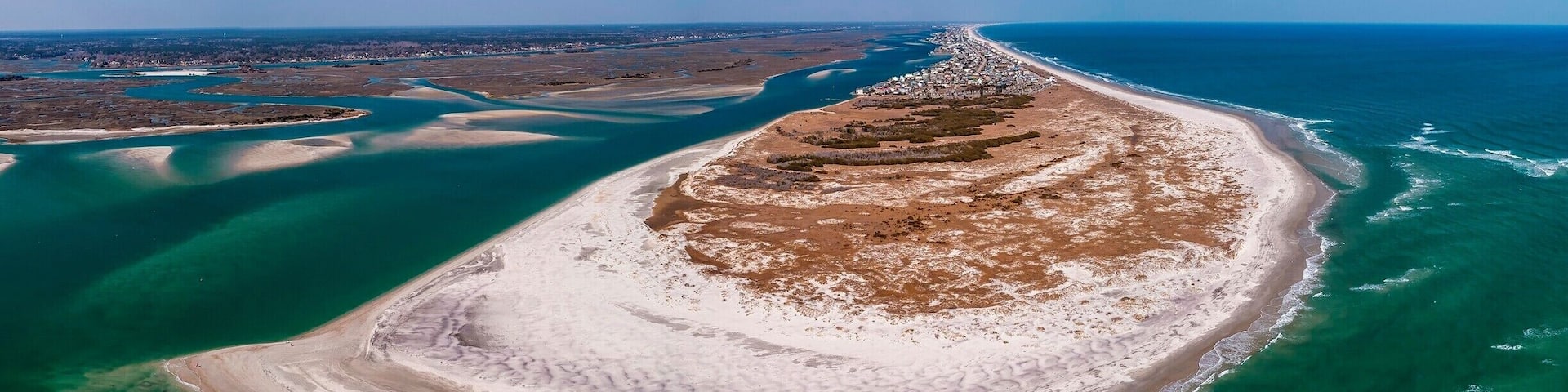 An aerial view of a crescent-shaped island with a sandy beach and clear turquoise waters.