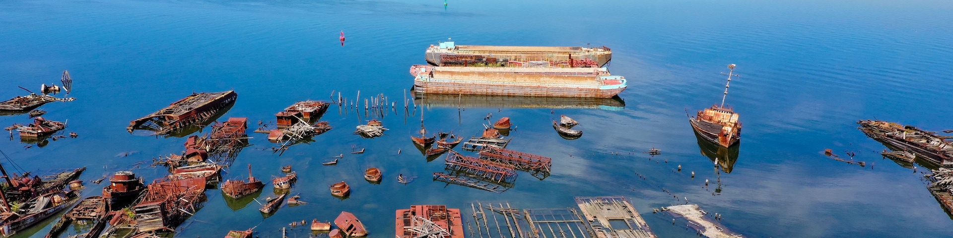 A large body of water with numerous sunken ships and boats, surrounded by industrial buildings and greenery.
