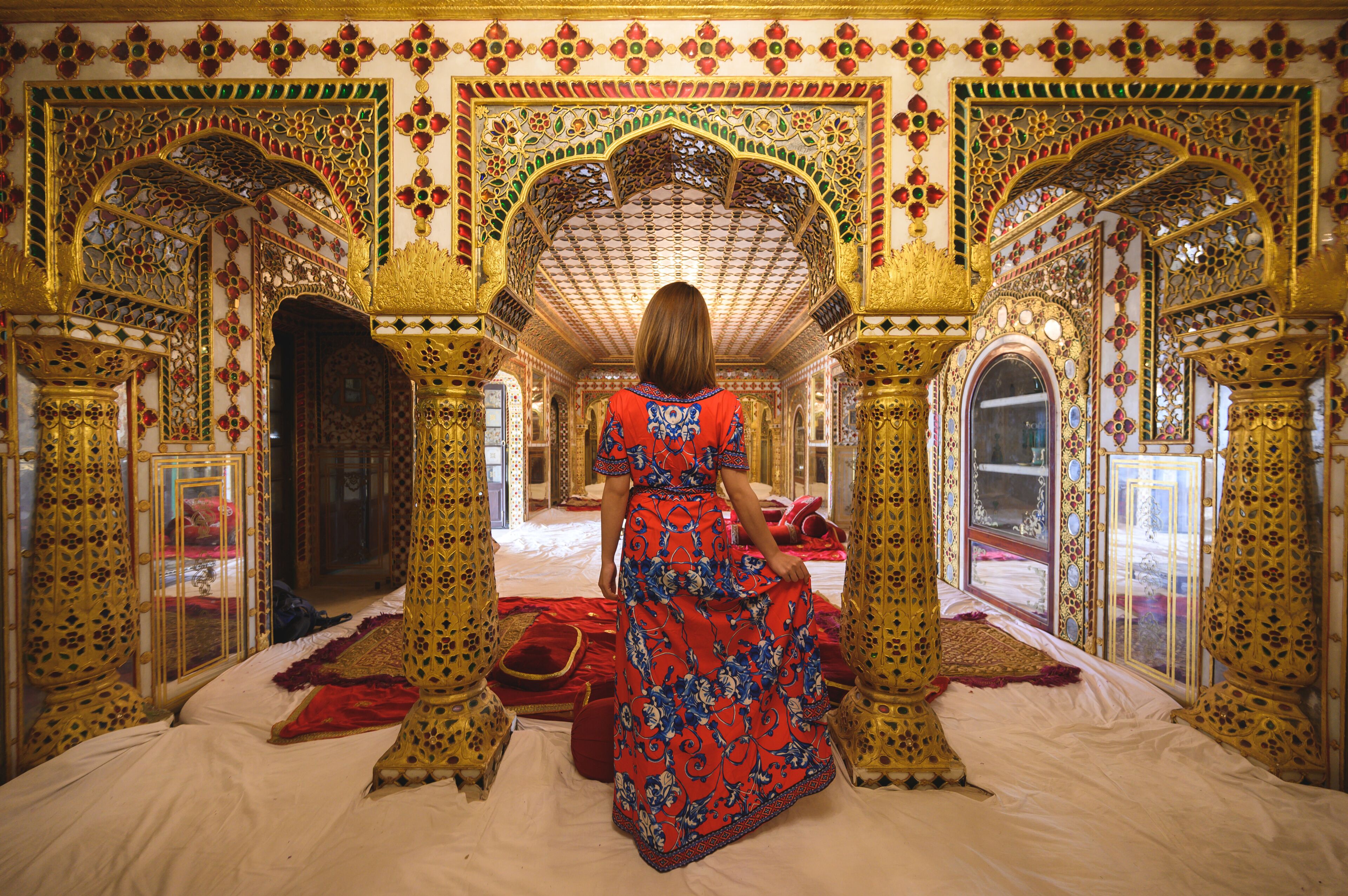 A richly decorated room with ornate arches and a patterned red and blue dress.