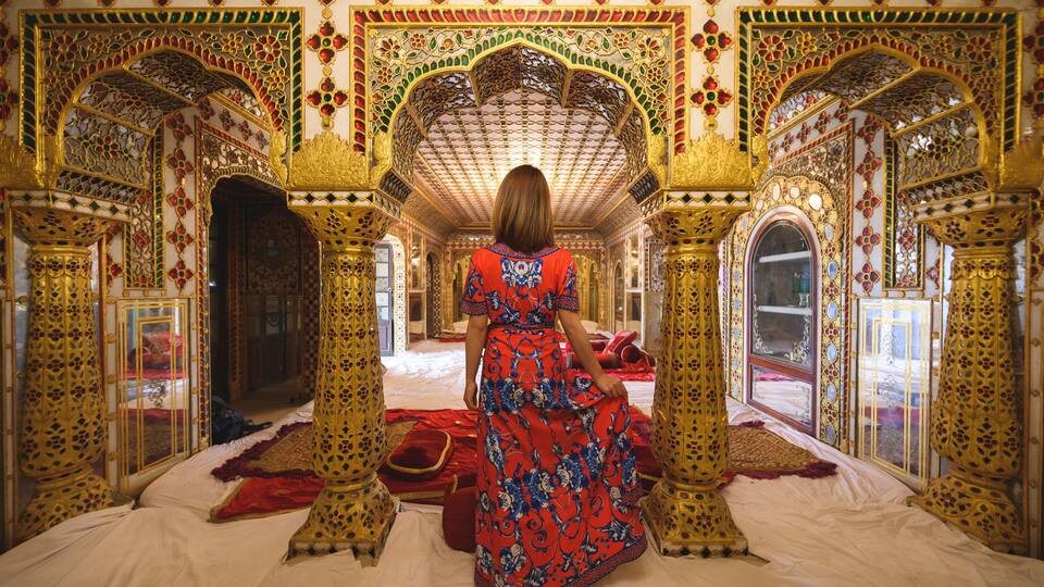 A richly decorated room with ornate arches and a patterned red and blue dress.