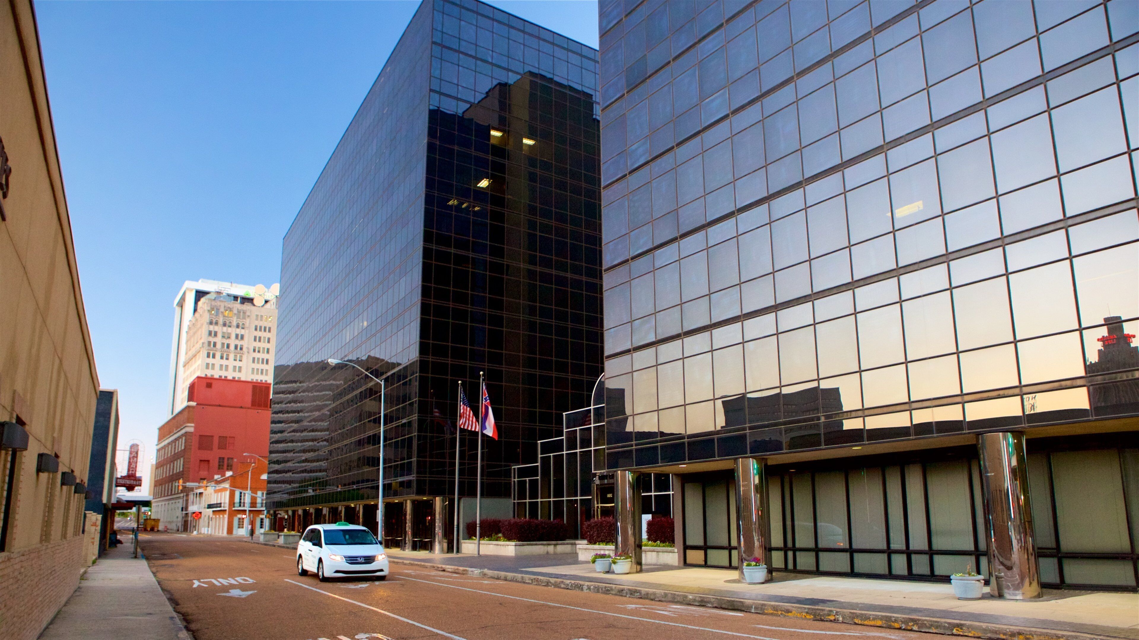 A city street with modern buildings, a white van, and American flags.