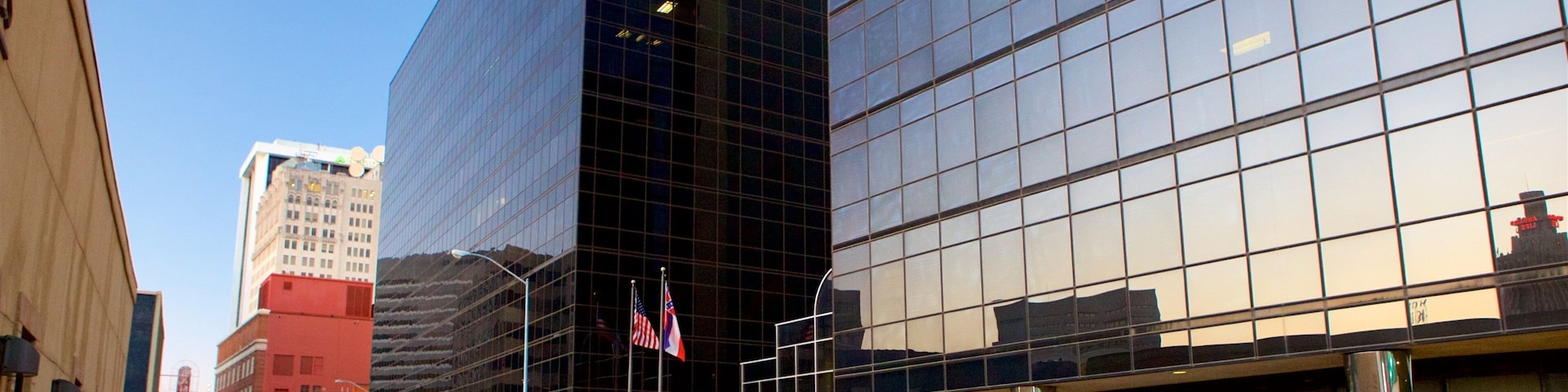 A city street with modern buildings, a white van, and American flags.