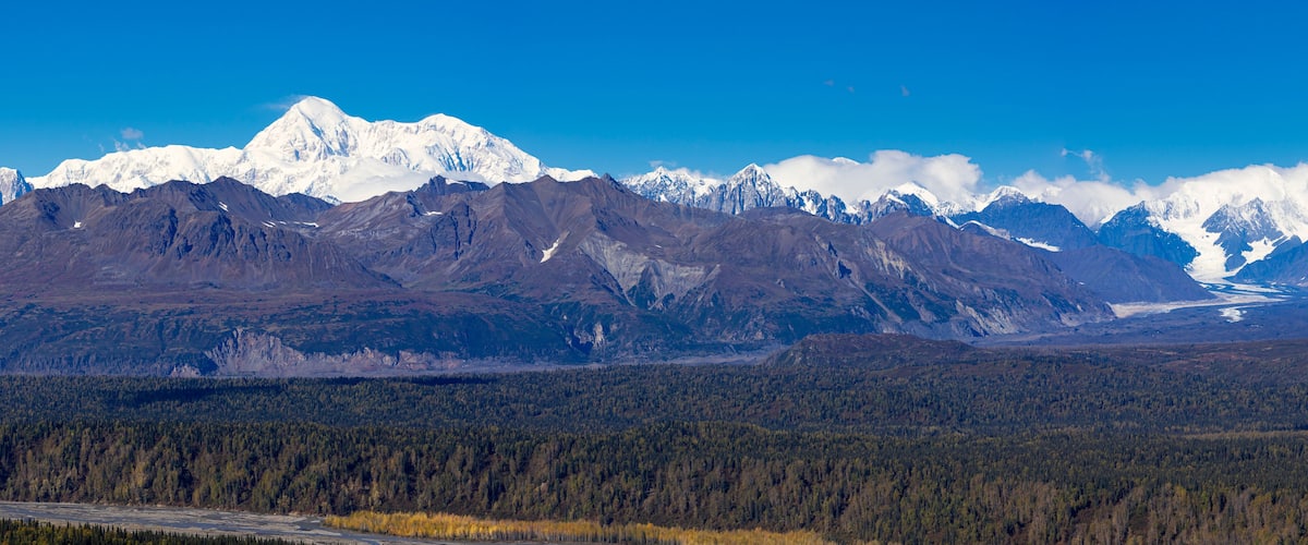 A snow-capped mountain range, dense forest, and a river.