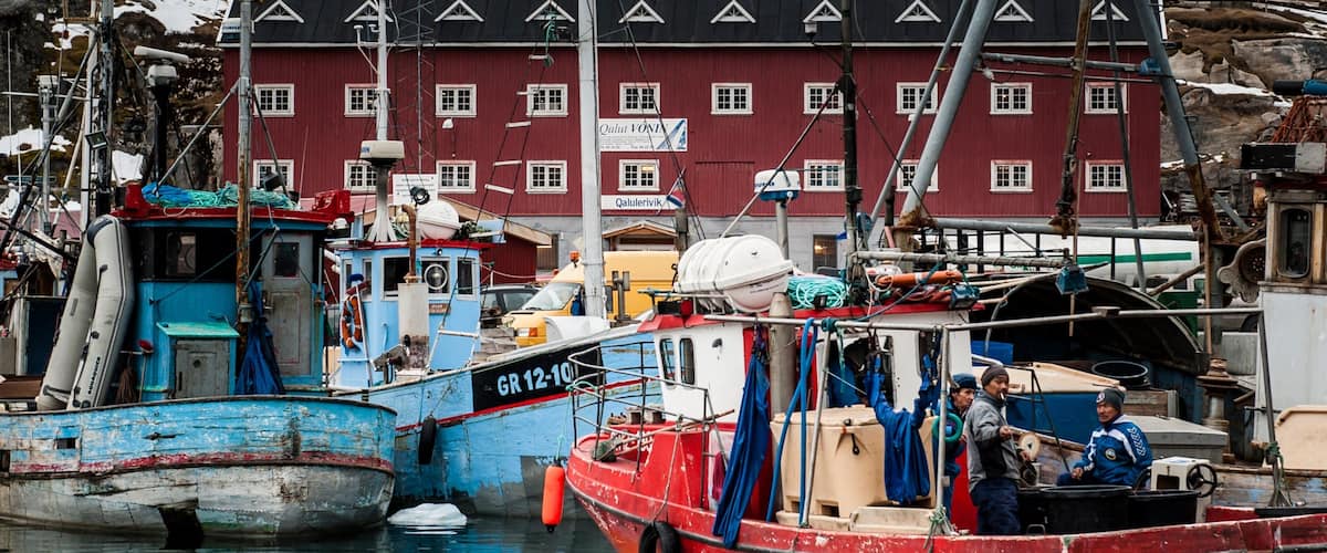 A harbor with several boats docked, a red building with windows, and a person on a boat.