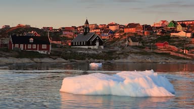 A coastal town with houses, a church, and an iceberg in the water.