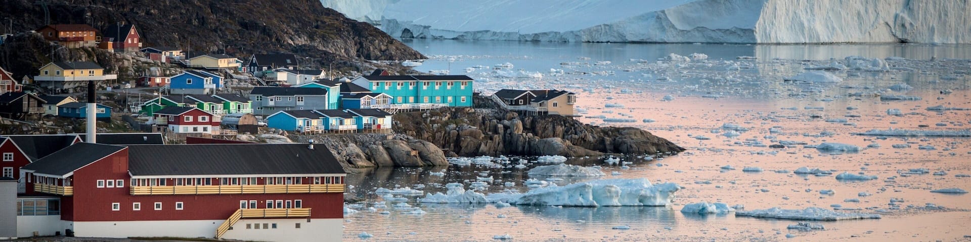 A coastal town with colorful buildings, a red boat, and icebergs in the background.