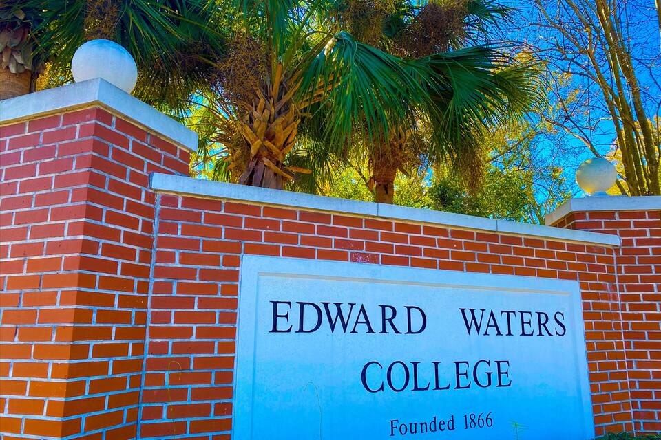 En murstensmur med et skilt for Edward Waters College, grundlagt i 1866, og palmer i baggrunden.