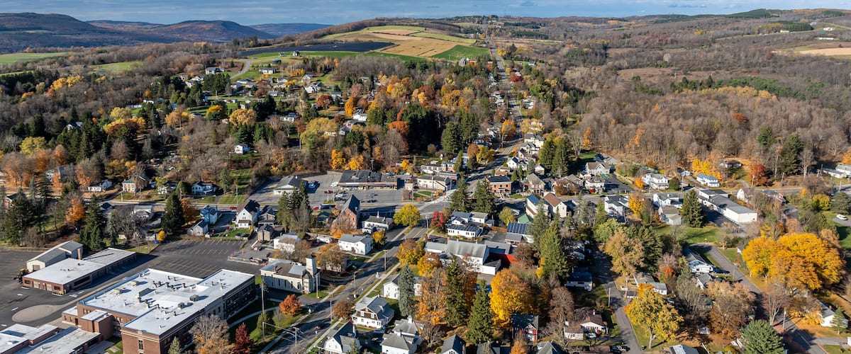 Eine Stadt, umgeben von herbstlich gefärbten Bäumen und sanften Hügeln.