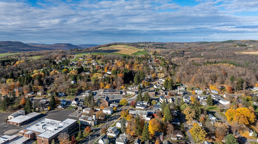 Uma cidade rodeada por árvores de tons outonais e colinas ondulantes.