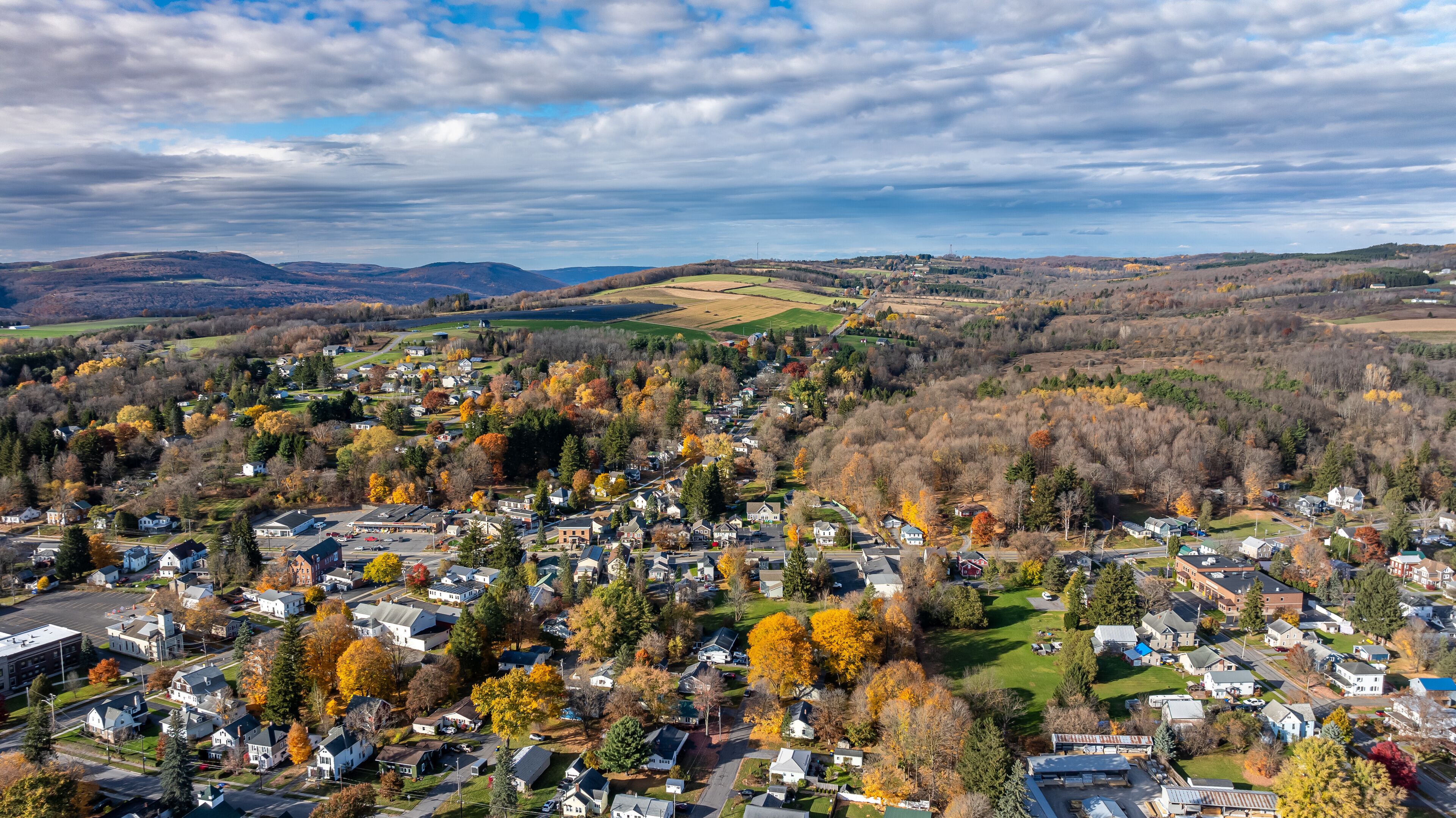A town with autumn foliage, a river, and rolling hills in the background.