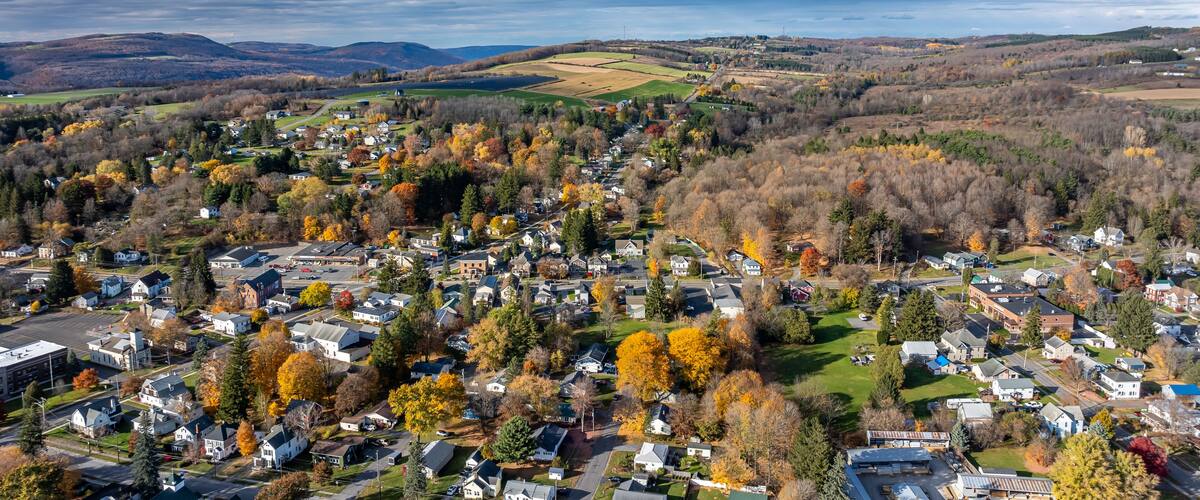 A town with autumn foliage, a river, and rolling hills in the background.