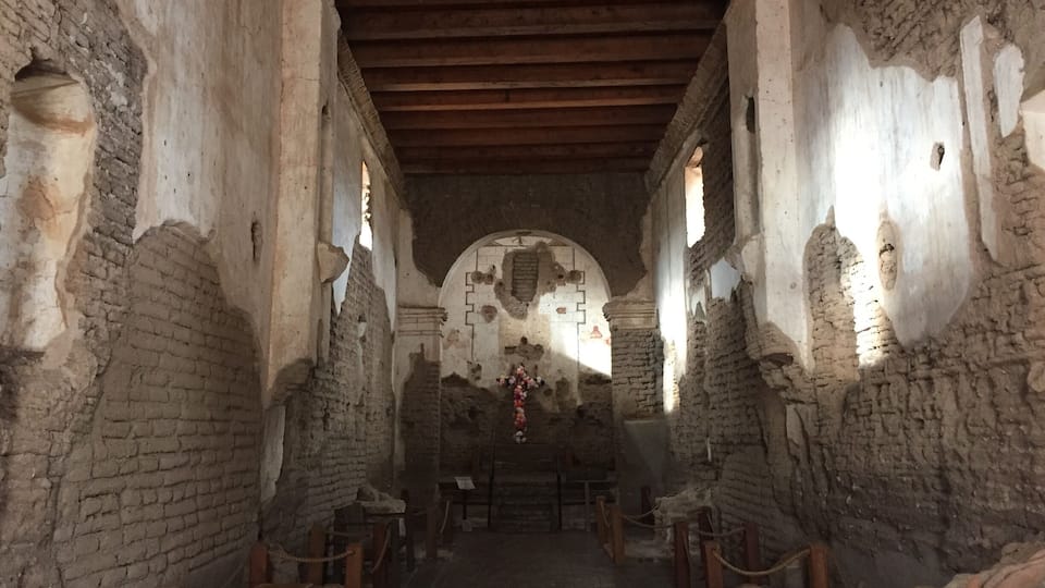 An ancient stone corridor with wooden benches and a central archway.